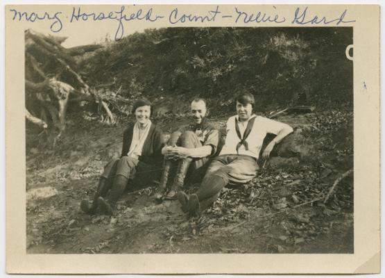 Marg. Horsefield, Count, Nellie Gard sitting in the ground with a bank and tree roots in the background