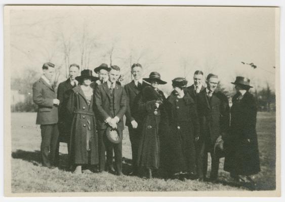 Group of University of Kentucky faculty, standing outdoors on grass with tree limbs in the background