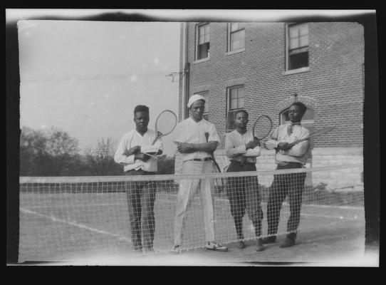 Negative of four unidentified men holding tennis rackets behind a net