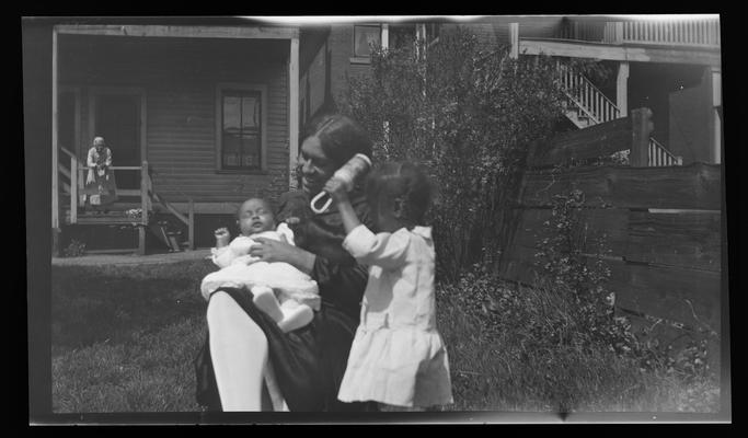 Negative of unidentified woman and two children in yard, unidentified woman on deck in background