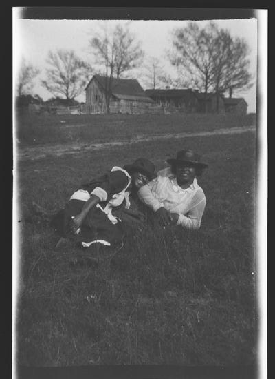 Negative of two unidentified women laying in a field