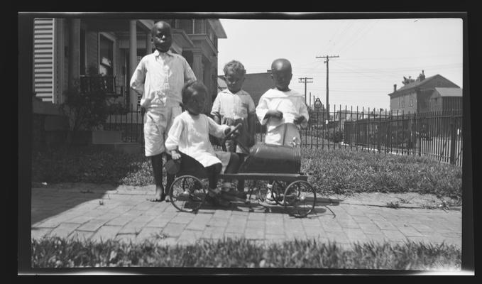 Negative of four unidentified children posing with a toy car