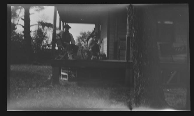 Negative of two unidentified persons on deck of a house