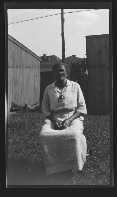 Negative of unidentified woman sitting in a chair in a yard