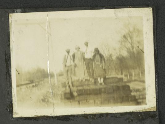 Page 7 [R]: Two unidentified black men and two women standing on a pile of cut logs