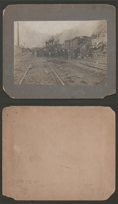 A train wreck; Damaged cars and track, with many men looking on