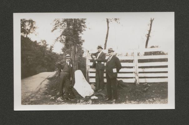 Three men standing by a fence