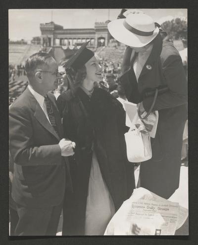 Young woman in academic robe with a man and woman, probably at college commencement. (Syracuse Daily Orange newspaper is visible)