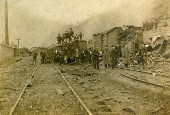 A train wreck; Damaged cars and track, with many men looking on