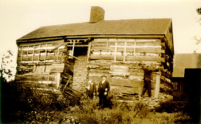 Three men in front of log cabin