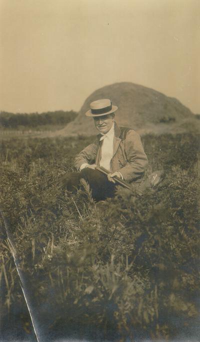 Samuel M. Wilson sitting in a field, holding a shotgun