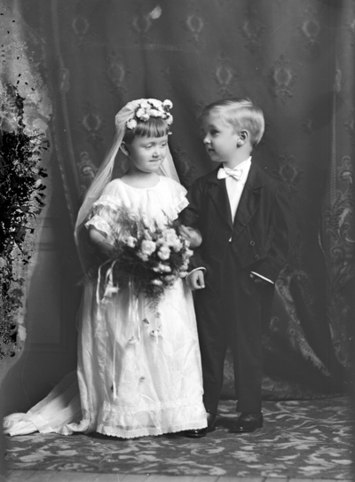 Full length group portrait of a standing boy and girl holding hands, identified as 