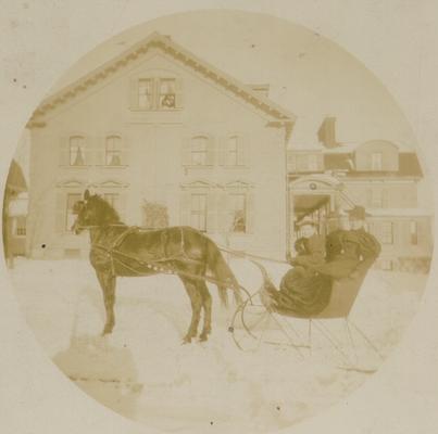 Horse and sled with two riders, snow, house in background. Manufacturers of the Kodak camera, Eastman Kodak Co.; Rochester, NY