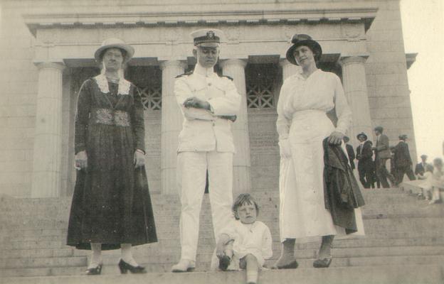 Naval officer, women, and a child on steps of a building