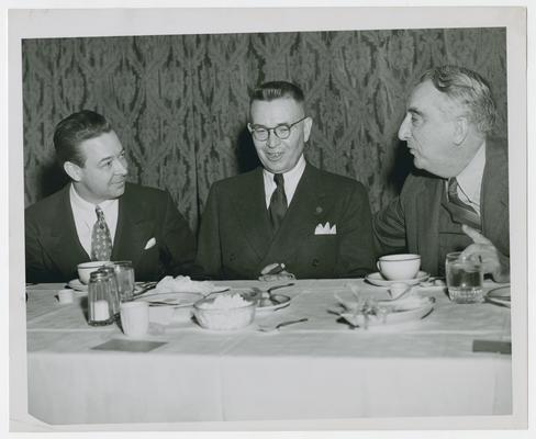 Secretary Vinson at dinner table with two unidentified men