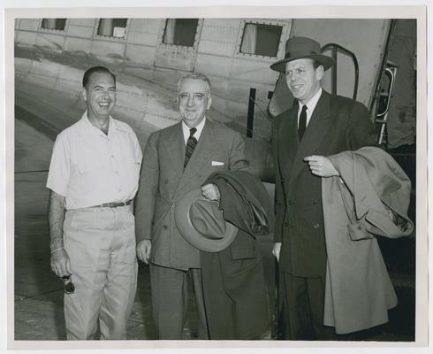Standing next to aircraft, left to right: Admiral Dennison, Chief Justice Vinson, and Clark Clifford
