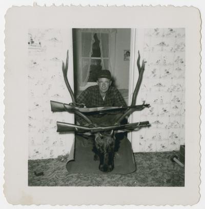 Hunter posed behind trophy head with two rifles hanging in antlers