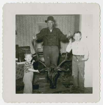 Hunter and two children hold trophy head by antlers