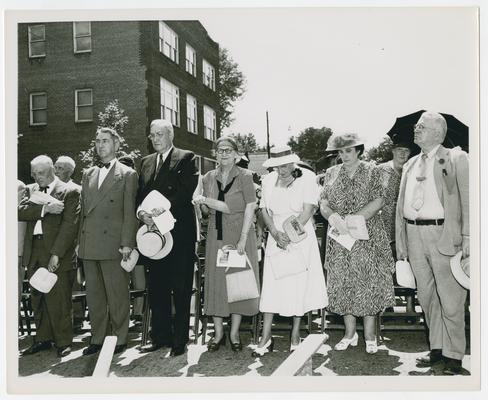 Crowd stands in front row of chairs at outdoor event