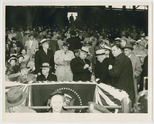 President Truman signs baseball at his box at Griffith Stadium. Chief Justice Vinson sits to the left of the President