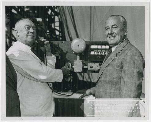 Page 16 of 38, two unidentified men at control panel, one of whom is on the phone