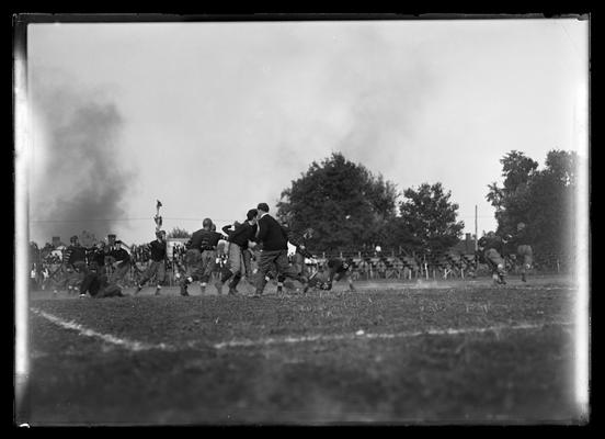 Football action, stripes on sleeves, men on telephone pole to left, two players on far right