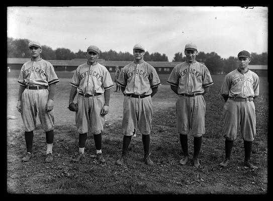 Five baseball players with long, low building in background