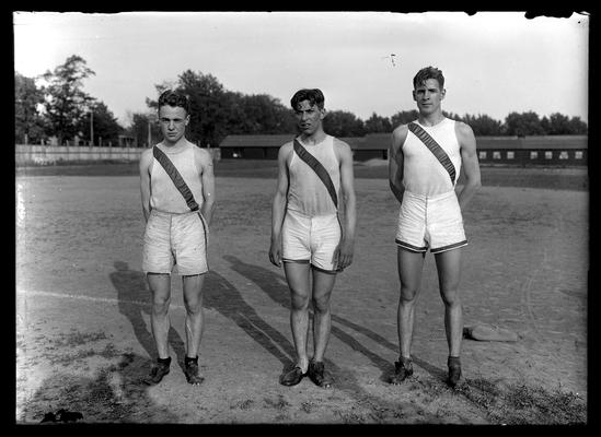 Track, three track men, long low building in background