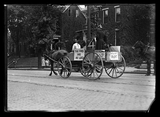 Horse-drawn wagon in parade, man in German helmet, signs on wagon