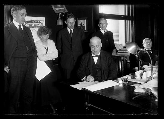 Governor A.O. Stanley signing the appropriation bill, President F.L. McVey, woman, R.C. Stoll, D.H. Peak, all seated, unknown man seated to right