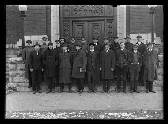 Twenty men on steps of Carnegie Library, all wearing caps or hats with exception of third from right