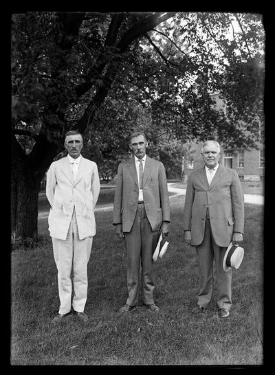 Three men, two with mustaches, building in background and large tree to left