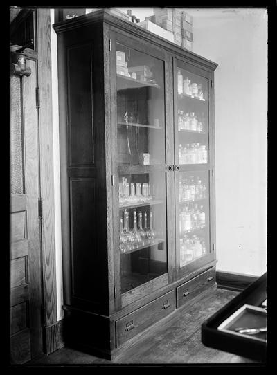 Tall cabinet with glass doors, reagents, bottles, etc inside