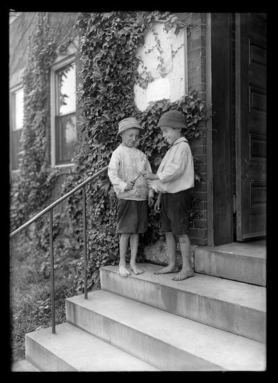 Two barefoot boys on the steps of ivy covered building