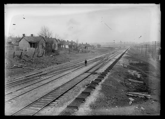 Man on railroad tracks, houses to left