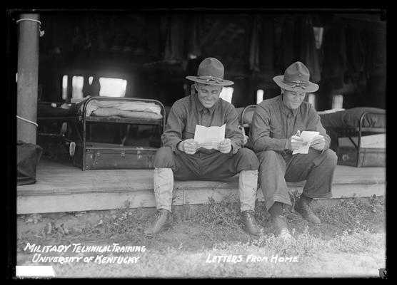 Two men, letters in hand, on edge of tent floor, cots in background, notation Letters from home, military technical training, University of Kentucky