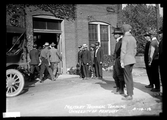 Some men entering brick, wide-doored building, four men by door looking on others watching