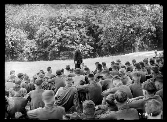 Listening to lecture, seated, man in front standing, steps of railroad memorail to right background