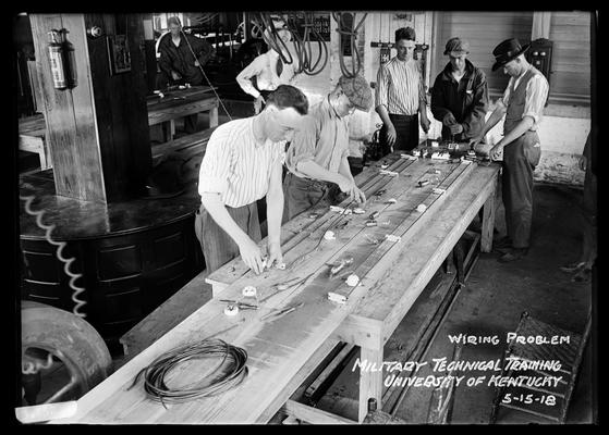 Seven men, some in hats, caps, long table, notation Wiring problems