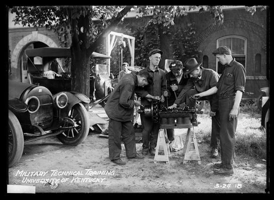 View outside auto shop, five men gathered around piece of equipment