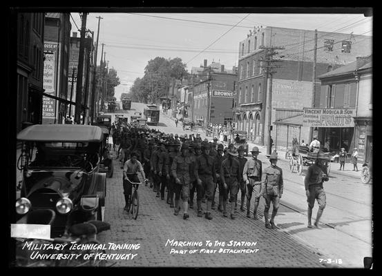 Front view of men marching, Lexington roller mills, Modica fruit, etc to right, notation Marching to the station, part of the first detachment