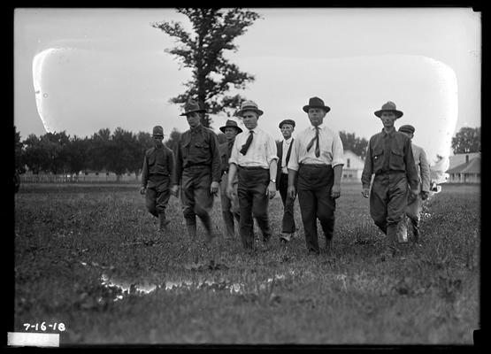 Eight men, civilian and military walking in field