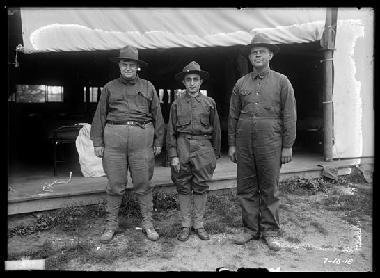 Two large men and one small man outside barracks, side of which is rolled up