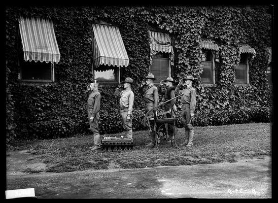 Five men in front of ivy covered building saluting, radio equipment