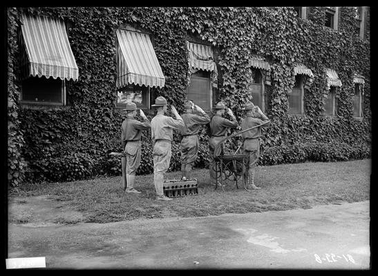 Five men in front of ivy covered building saluting, radio equipment