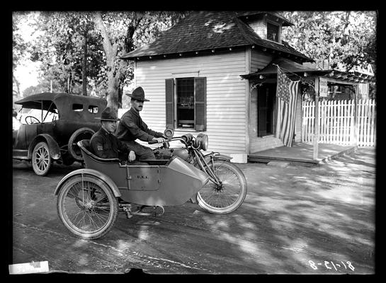 Two men, motorcycle, side car, small building with flag, notation Quick messenger service
