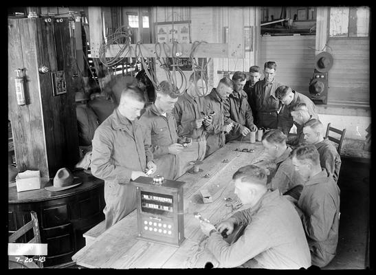 Electrical, men around table with dry cells, bells, etc, instrument on table to left of picture