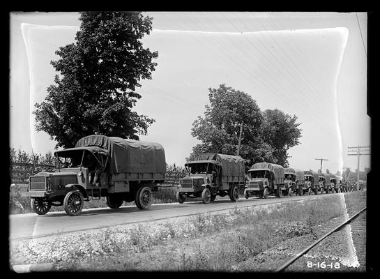 Long line of trucks on road by railroad tracks, notation Truck train