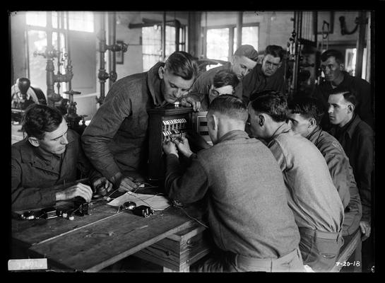 Several men around table, instrument with numbers, notation Exploring an annunciator