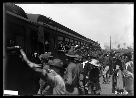 People at station by side of train, soldiers inside waving, breaking up camp, train logo Baltimore and Ohio visible